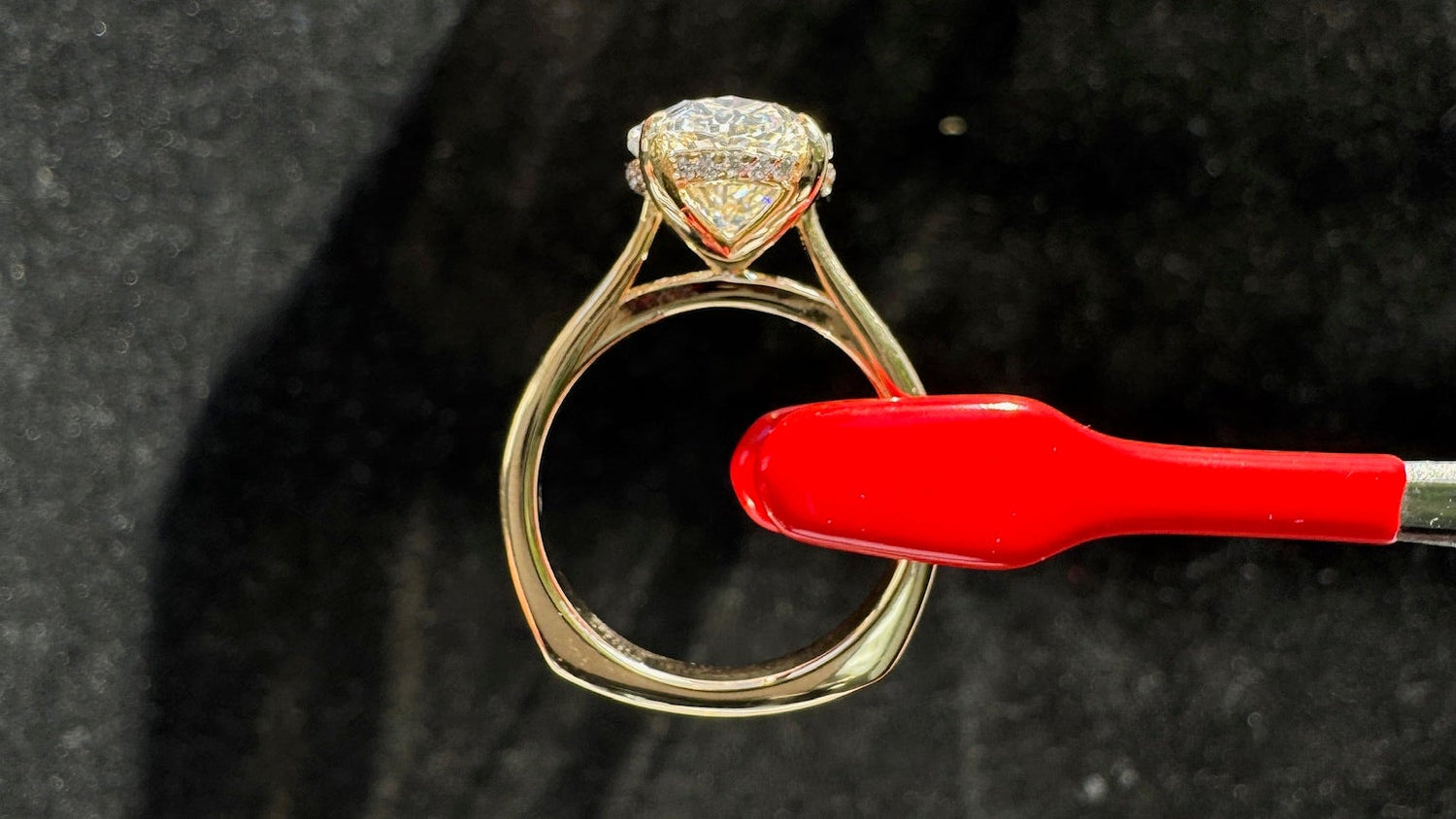 Gold ring with a diamond being held by a red tool on a black background
