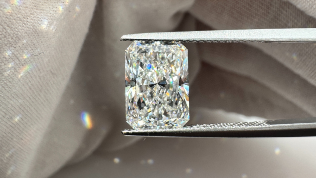 Diamond held between tweezers against a soft fabric background